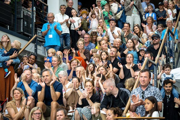 Et tætpakket publikum med børn og voksne klapper og smiler på trappen i Kulturhuset under en optræden til Sløngeldagene.